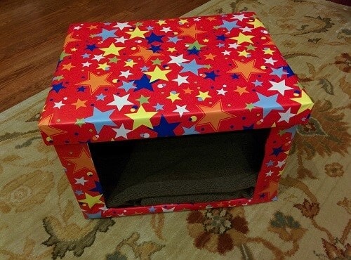 DIY Cardboard cat bed covered in red fabric with different colored stars.
