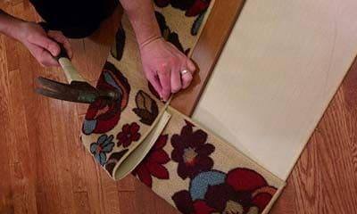 Woman hammering tack nails into board to secure a flowered area rug to wood for cat scratch board.