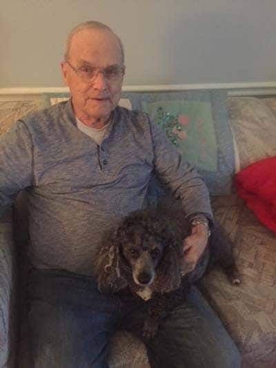 Paul with his arm around his dog Tuxedo, sitting on the couch.