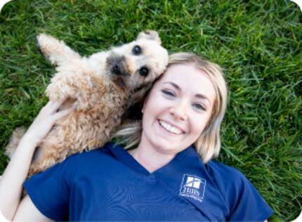 A small dog lying in the grass next to a Hill's researcher
